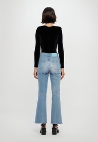 Bodysuit negro de manga larga con cremallera en la espalda, combinado con unos jeans acampanados azules claros que tienen un parche azul en la cintura y un desvanecimiento sutil.
