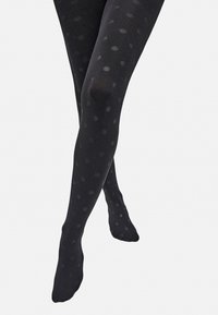 Medias negras con lunares, de textura suave, con un diseño semitranslúcido y grandes patrones circulares dispuestos de manera uniforme.