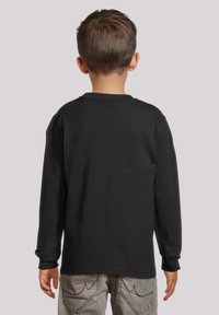 Langärmliges schwarzes Baumwoll-T-Shirt mit Rundhalsausschnitt, einfarbigem Rücken und enganliegenden Bündchen, kombiniert mit grauen Hosen mit dekorativen Nähten.