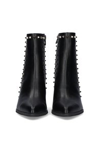 Botines de cuero negro con puntera afilada, textura suave y tachuelas metálicas en los laterales como detalle.