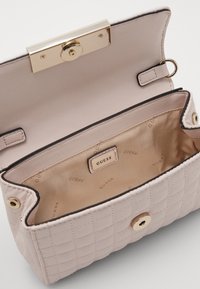 Lyserød quilted håndtaske med en guldfarvet lukning, der har en glat indvendig foret og et mærke. Åbent design fremviser det indvendige rum.