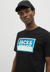 Sort bomulds T-shirt med et iøjnefaldende blåt og hvidt "JACK & JONES" grafik på fronten. Kortærmet og rund halsudskæring.