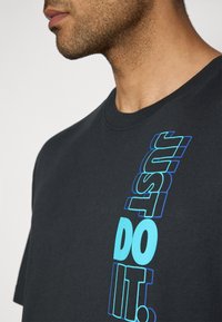 Sort bomulds T-shirt med vertikal tekst "JUST DO IT." i blå og cyan, rund hals, korte ærmer og en blød tekstur.