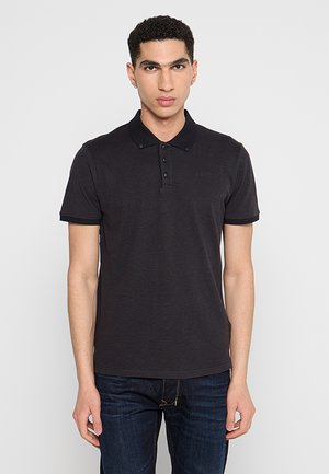 Polo noir en coton, avec un col, une patte de boutonnage à trois boutons et un discret logo sur la poitrine. Associé à un jean en denim foncé.