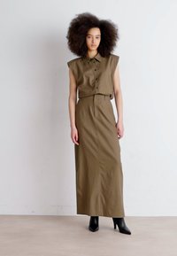 Completo due pezzi color khaki composto da una camicia a maniche corte con bottoni e una gonna lunga. Indossato con tacchi alti neri a punta. Tessuto morbido.
