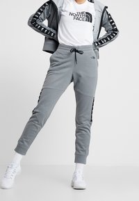 Grå atletiska joggers med elastisk midja, dragsko och kontrasterande svarta sidostråkar med logotyper. I kombination med en vit t-shirt med logo.