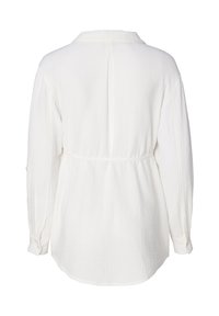 Chemise blanche à col classique avec manches longues, en tissu texturé, taille cintrée et poignets à boutons. Présente un ourlet arrondi.