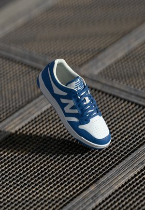 Pantofii sport în nuanțe de albastru și alb, cu vârful perforat, dotati cu un guler căptușit, închidere cu șireturi și un logo 'N' proeminent pe lateral.