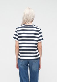 Camiseta de algodón a rayas en azul marino y blanco, mangas cortas, cuello redondo, vista trasera. Combinada con vaqueros holgados de mezclilla.