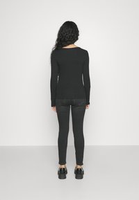 Μαύρη μπλούζα με μακριά μανίκια συνδυασμένη με σκούρες γκρι skinny jeans και χοντρές μαύρες πλατφόρμες, απεικονισμένη από πίσω σε ουδέτερο φόντο.