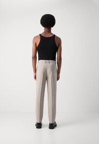 Black tank top worn with light gray tailored trousers, featuring a straight cut and belt loops. Black loafers complete the outfit.