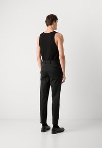 Black ribbed tank top with slim black trousers. The trousers feature a tailored fit, side pockets, and a smooth finish. Black dress shoes complete the look.