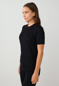 Top corto nero a maniche corte realizzato in un materiale testurizzato e scintillante. Presenta un collo rotondo e una silhouette aderente. Indossato con pantaloni neri.