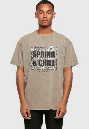Beige oversized bomulds t-shirt med en blomstergrafik og teksten "SPRING & CHILL" i sort samt "ONLY GOOD VIBES" nedenfor.