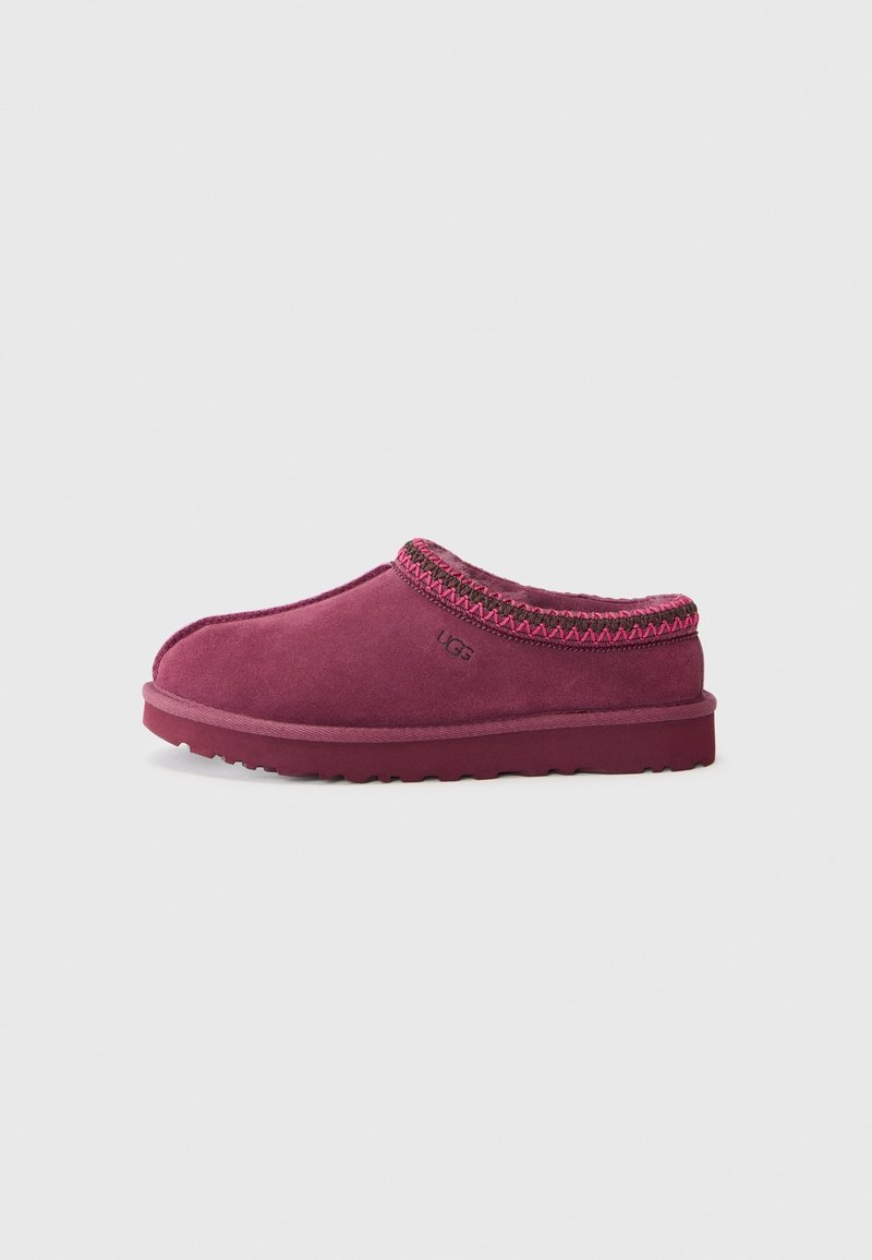 Chausson en daim couleur prune à enfiler, avec bordure cousue et logo UGG imprimé sur le côté, semelle plate et bout fermé arrondi.