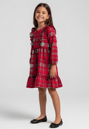 Czerwona sukienka w kratę z długimi rękawami, falbankami na ramionach i rozkloszowanym dołem. Charakteryzuje się czarno-białym wzorem w kratę. Zestawiona z czarnymi balerinami.