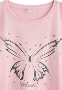 Rosa skjorte med sort stiliseret sommerfugledesign, sølvnittebesætninger og ordet "Amore" skrevet under sommerfuglen.