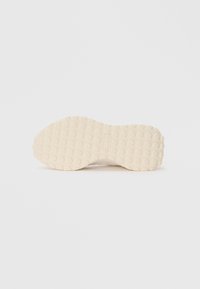 Semelle d'une sneaker, texturée avec des motifs hexagonaux, de couleur crème. Finition lisse, forme arrondie, marque minimalement visible.