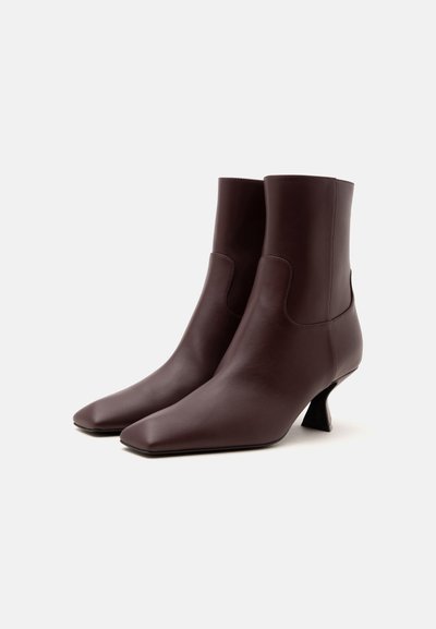 Paire de bottines en cuir marron foncé à bouts pointus et talons évasés sur fond blanc uni.
