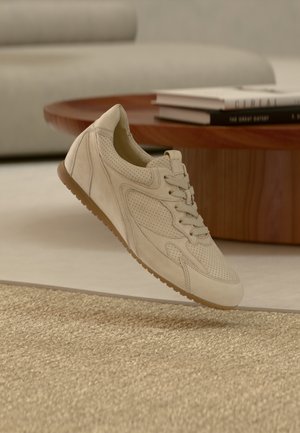 Beiger Sneaker mit perforiertem Design, flachen Schnürsenkeln und einer Sohle aus Kaugummi-Gummi. Verfügt über glattes Veloursleder und eine geformte, leichte Zwischensohle für zusätzlichen Halt.