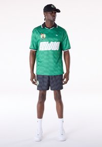 Camiseta verde con un patrón texturizado, detalles en blanco, logo en el pecho; combinada con pantalones cortos oscuros que presentan un logo y diseño con texto.