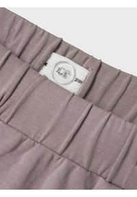 Tessuto viola chiaro con texture a righe, caratterizzato da un elastico bianco con un dettaglio di bottone cucito e pieghe in vita.