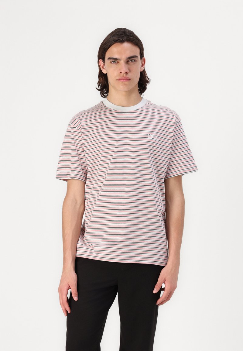Cotton T-shirt featuring horizontal red, blue, and white stripes, a crew neckline, and a small logo on the chest. Worn with black pants.