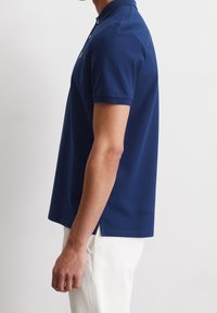 Tmavě modré polokošile s límečkem na tři knoflíky, krátkými rukávy, bočními rozparky a hladkou texturou. Doplněno minimalistickým designem.