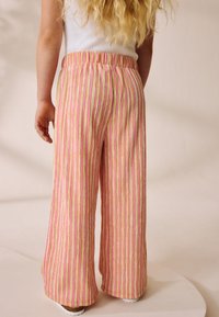 Pantalon large rayé rose et jaune avec une taille élastique, présentant un tissu texturé qui contraste avec des chaussures blanches lisses.