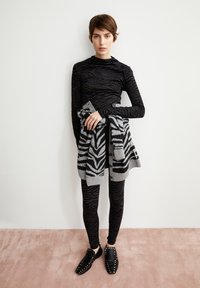 Langärmliges schwarzes Oberteil mit wellenförmigem Muster, kombiniert mit einem grauen Cardigan im Zebra-Muster, schwarzen Leggings und schwarzen Slippern mit Nieten.