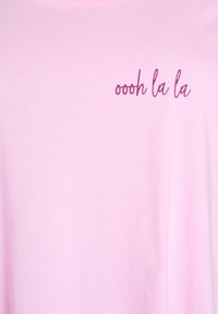 T-shirt in cotone rosa con la scritta "oooh la la" in corsivo rosa scuro. Il tessuto ha una texture liscia e una vestibilità comoda.