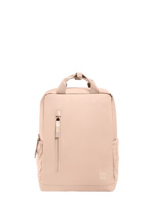 Sac à dos carré beige avec une poignée supérieure, une poche zippée verticale à l'avant, des poches latérales, et un logo discret "GOT BAG" près du coin inférieur droit.