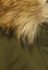 Pelskant med blandede brune og blonde farver på kraven af en olivengrøn vinterfrakke.