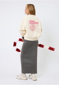 Sweat-shirt crème avec texte imprimé rose et motif floral au dos, associé à une jupe gris foncé pailletée et des baskets claires.