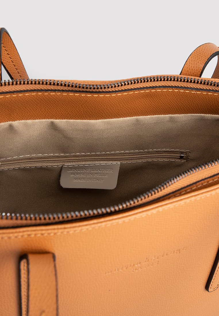 Interno di una borsa in pelle tan con una fodera in tessuto morbido, dotata di una tasca con zip e un'etichetta che afferma "pelle genuina, made in Italy."