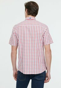 Chemise à manches courtes à motif carreaux rouges et blancs, avec un accent bleu au col, fabriquée en tissu léger.