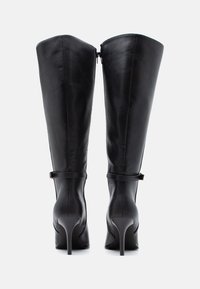 Μαύρες δερμάτινες μπότες έως το γόνατο με εφαρμοστό σχέδιο, μυτερή μύτη και ψηλές στιλέτο γόβες. Διαθέτουν πίσω φερμουάρ και λεπτομέρεια με λουρί στον αστράγαλο.