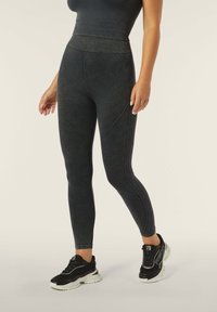 Leggings neri a vita alta con vita a coste, tessuto testurizzato e cuciture a contrasto, abbinati a sneakers nere con suole bianche.