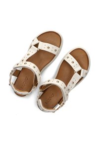 Bílé sandály s dekorativními cvočky, polstrovanou hnědou stélkou a designem s křížovými popruhy, s nastavovacími sponami pro lepší přizpůsobení.