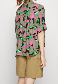 Camicia a maniche corte con un motivo astratto colorato in rosa, verde e nero, caratterizzata da una vestibilità ampia e un tessuto leggero e testurizzato.