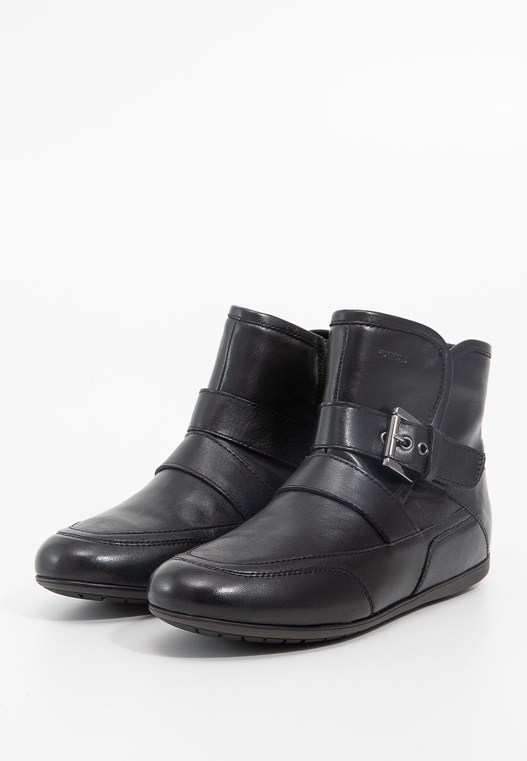 Bottines en cuir noir avec semelle plate, design à coutures diagonales et boucle décorative sur le côté. Texture lisse, style minimaliste.