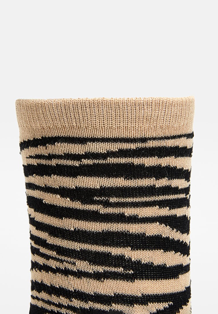 Calcetín de algodón beige con un patrón de rayas negras, que presenta un puño acanalado y una textura suave. El diseño imita un motivo de rayas de cebra.