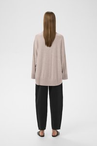 Ljusrosa, överstor stickad tröja med ribbade muddar, i kombination med svarta, löst sittande byxor och platta sandaler, sedd bakifrån.