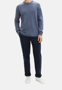 Pull bleu tricoté à col rond, associé à un pantalon bleu marine et des baskets blanches. Le pull a des manches longues avec des poignets et un ourlet côtelés.