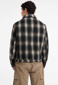 Karirani sako u crnoj, bež i svijetloplavoj boji. Napravljen od mekanog materijala s ovratnikom i dugmadi na rukavima. Pogled s leđa prikazuje kroj prilagođen tijelu.