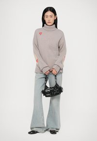 Šviesiai pilkas per didelis megztinis su aukštu kaklu, su raudonais širdelės stilizavimais ir priekinėmis kišenėmis. Suderintas su plačiomis džinsinėmis kelnėmis ir juodu rankiniu krepšiu.