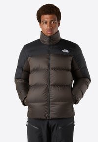 Tmavě hnědá a černá péřová bunda s vysokým límcem, předním zipem a logem na hrudi; silné švy a polstrovaný design pro teplo.