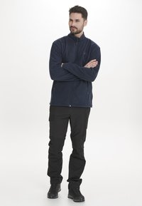 Marinfärgad fleecejacka med hög krage och full dragkedja, kombinerad med svarta cargobyxor med fickor och svarta vandringsskor.