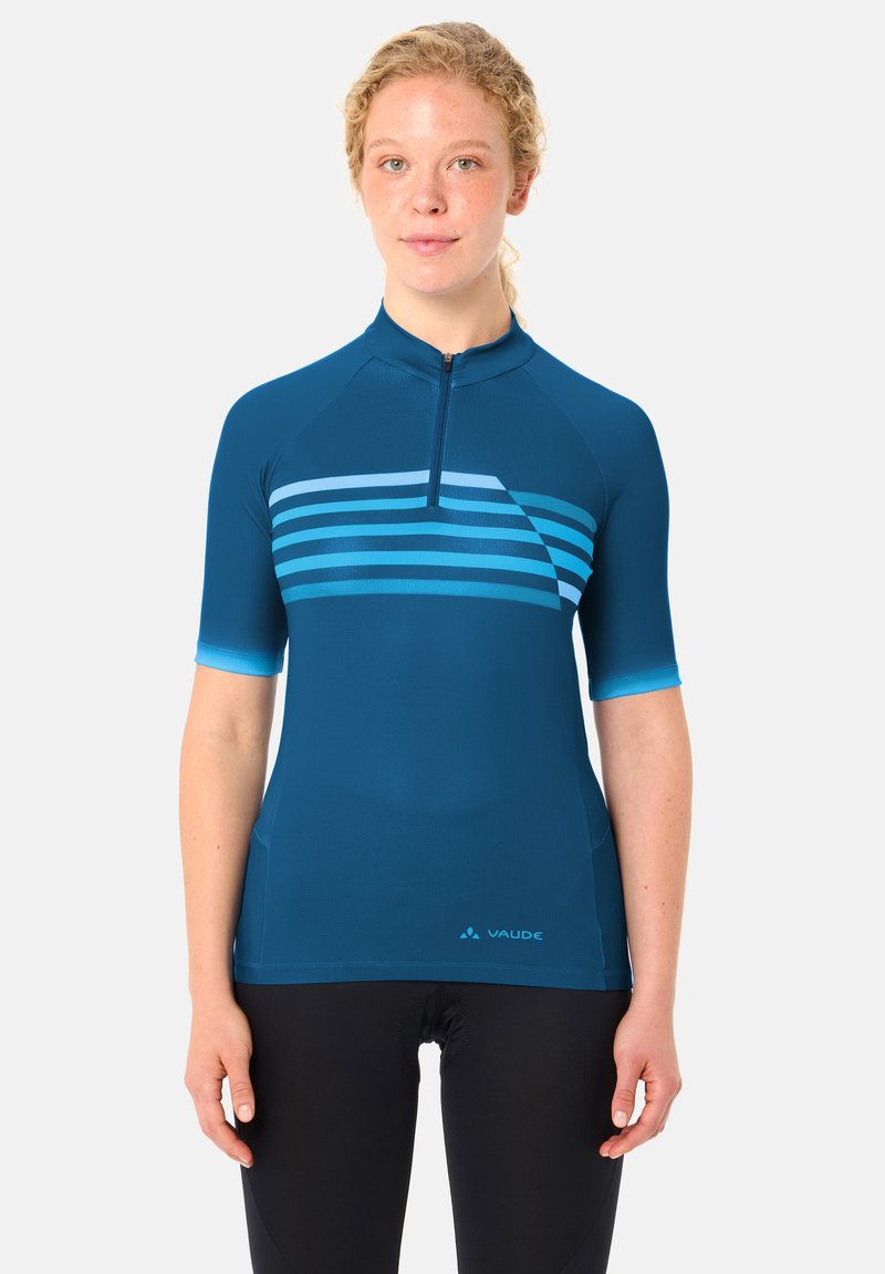 Femme portant un maillot de cyclisme bleu ajusté avec une fermeture éclair courte et des rayures horizontales, associé à un cuissard de cyclisme noir.