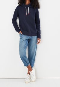 Námořnická mikina s límcem a bílými šňůrkami, spárovaná se světle modrými, volně střiženými džíny a bílými teniskami.